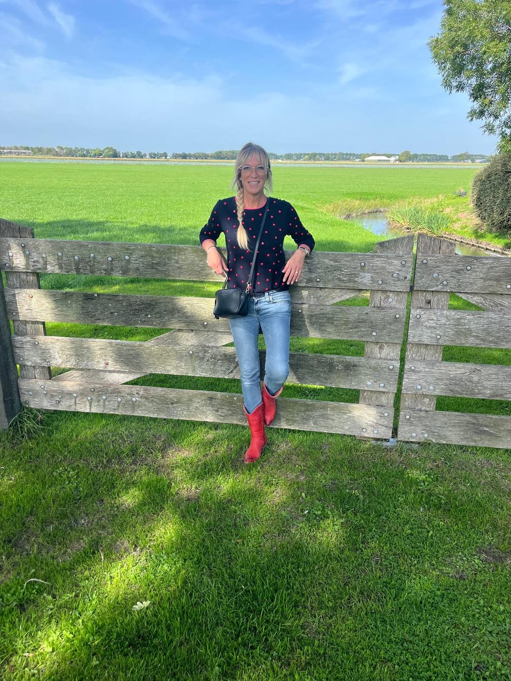 Thea leunt in rode laarzen tegen een houten hek met weiland erachter